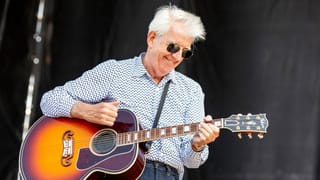 Ein Mann mit weissem Haar steht mit einer Gitarre auf der Bühne. Ein Mann mit weissem Haar steht mit einer Gitarre auf der Bühne.