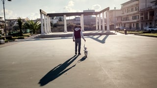 Ein Junge führt seinen Hund spazieren, im Hintergrund eine Art Torbogen.