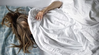Ein Kind liegt im Bett, die weisse Decke über den Kopf gezogen.