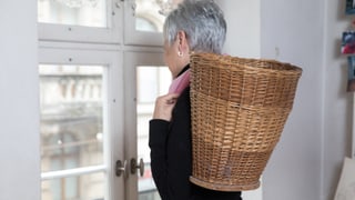Eine Frau schaut aus dem Fenster. Auf ihrem Rücken trägt sie einen Korb. Eine Frau schaut aus dem Fenster. Auf ihrem Rücken trägt sie einen Korb.