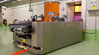 Ein Transportsystem fährt ein oranges Fass mit radioaktiven Abfällen zum Tor des Plasmaofens.