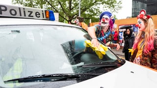 Clowns putzen die Frontscheibe eines Polizeiautos