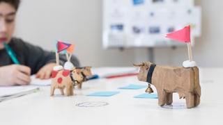 Drei Kühe aus Holz stehen auf einem Tisch. Auf den Figuren sind kleine Fähnchen angebracht. Drei Kühe aus Holz stehen auf einem Tisch. Auf den Figuren sind kleine Fähnchen angebracht.