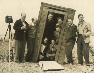 Eine Gruppe Studenten posiert in einem schrägen Holzschuppen.