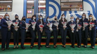 12 Frauen in Uniform stehen mit Rosensträussen in den Händen vor einem Zug.