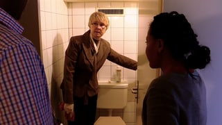 Ein Mann zeigt zwei Personen eine Toilette.