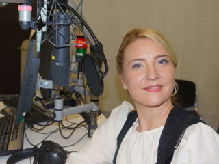 Frau in Tracht vor Microfon in Radiostudio.