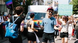 mehrere junge Menschen tanzen und halten Plakate hoch und Regenbogen-Flaggen