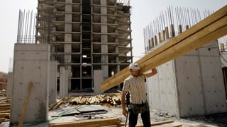Ein Arbeiter trägt einen grossen Balken über eine der zahlreichen Baustellen in Erbil.