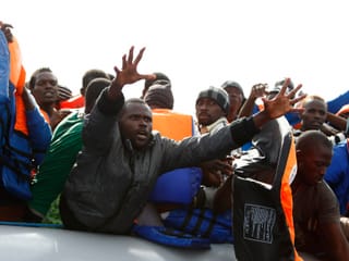 Flüchtlinge auf einem Boot strecken ihre Arme den Helfern entgegen.