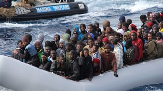 Schlauchboot mit Migranten. Im Hintergrund ein Boot der italienischen Marine.