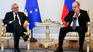 Jean-Claude Juncker und Vladimir Putin sitzen vor EU- und Russlandfahne.