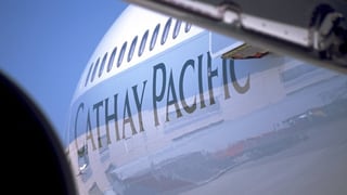Blick vom Boden aus zwischen Flügel und Triebwerk auf den Schriftzug "Cathay Pacific" an einem Aribus