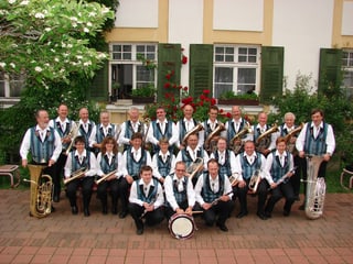 Die Musikantinnen und Musikanten der Frienisberger Blasmusikanten in weissen Hemden und hellblauer Weste auf einem Gruppenbild im Freien.