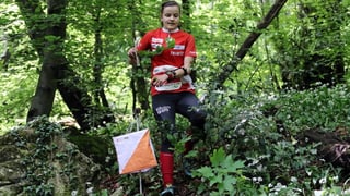 Sofie Bachmann im Dress der Nationalmannschaft rennt durch den Wald. Neben ihr ein OL-Posten bestehend aus einer kleinen Flagge.
