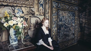 Emma Stone sitzt als Kammerzofe Abigail auf einem Stuhl im Palast. Emma Stone sitzt als Kammerzofe Abigail auf einem Stuhl im Palast.
