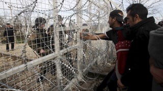 Flüchtlinge blicken durch einen Zaun hindurch zwei Polizisten an. Flüchtlinge blicken durch einen Zaun hindurch zwei Polizisten an.