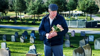 Mann steht mit Blumen auf Friedhof. 
