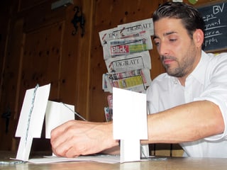 Mann am Tisch, vor sich aufrecht stehende, weisse Papierstreifen.
