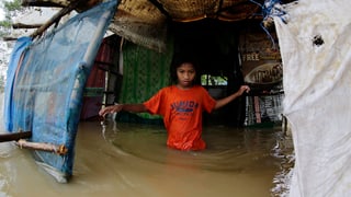 Ein Kind auf den Philippinen. Es steht hüfttief im Wasser, vor seinem Daheim.