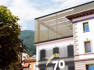Teil eines grossen Gebäudes. Auf dem Dach ein halbtransparenter Aufbau mit goldenen Elementen. Am Gebäude hängt eine Fanhe mit einem springenden Leoparden und der Zahl 70.