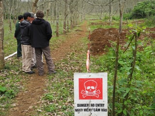 Männer stehen neben einem Feld, vor dem ein Schild steht, u.a. mit der engl. Aufschrift: Danger! No entry