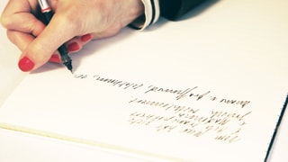 Frauenhand mit roten Fingernägeln beim Schreiben