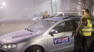Fahrerinnen stehen im Nebel bei einem Auto mit Nez Rouge-Aufkleber