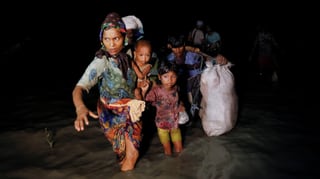 Eine Frau mit Kindern sowie ein schwer beladener Mann waten bei Nacht durchs knietiefe Wassesr.