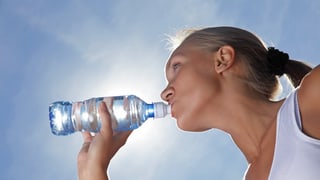 Frau an Sonne trinkt Wasser aus einer Plastikflasche