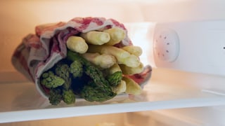 Grüner und weisser Spargel in einem Tuch im Kühlschrank.