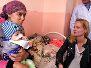 Sarina Arnold kniet vor dem Spitalbett. Darauf sitzen Mutter mit kleinem Abdulla auf dem Schoss. Er hat ein grosses Pflaster auf der Nase. Der Arzt beobachtet die ganze Situation.