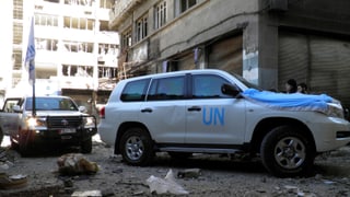 Zwei Autos der UNO fahren durch ein zerstörtes Quartier.