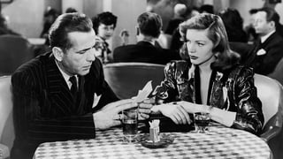 Ein Mann und eine Frau sitzen an einem Café-Tisch und lesen einen Zettel.