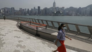 Frau mit Mundschutz läuft vor der Hongkonger Skyline
