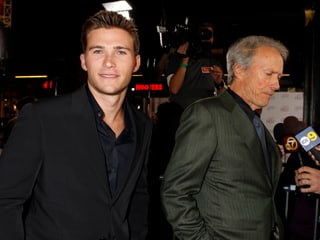 Scott Eastwood für die Kamera posierend, Clint Eastwood gibt im Hintergrund ein Interview.