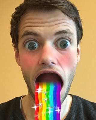 Ein unglaublich gut aussehender Mann im besten Alter kotzt einen Regenbogen und macht dazu grosse Augen.