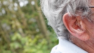 Ohr eines alten Menschen, der ein Hörgerät trägt.