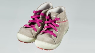 Ein paar graue Kinderschuhe mit rosa Schuhbändeln. 