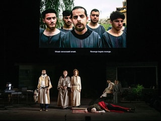 Eine Theaterbühne: Vorne sind fünf SchauspielerInnen, auf dem Bildschirm hinten sind fünf Darsteller. Eine Theaterbühne: Vorne sind fünf SchauspielerInnen, auf dem Bildschirm hinten sind fünf Darsteller.