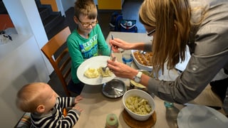 Mutter schöpft zwei kleinen Kindern Essen am Tisch