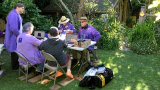 Fünf Herren mit violetten Jacken in einem Garten. 