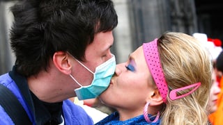 Ein Liebespaar küsst sich. Der Mann trägt einen medizinischen Anti-Grippenviren-Mundschutz.