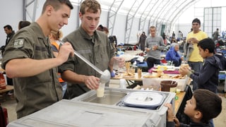 Zwei Bundesheer-Soldaten schöpfen Flüchtlingen das Essen aus.