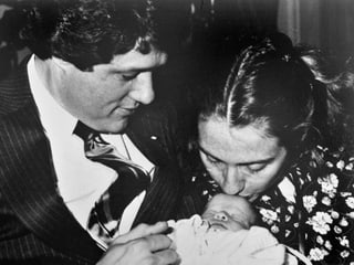 Hillary Clinton küsst ihre neugeborene Tochter, die Bill Clinton im Arm hält.