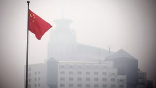 Eine chinesische Fahne weht im Smog, dahinter ist eine Gebäude zu sehen.