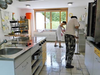 Zwei Menschen putzen Boden in einer grossen Küche.