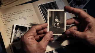 Eine Hand hält ein altes Foto eines kleines Kindes.