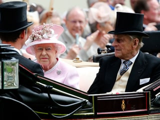 Die Queen mit pinkem Hut sitzt neben Prinz Philip in einer Kutsche.