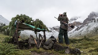 Jäger mit Feldstecher inmitten leicht verschneiter Berge